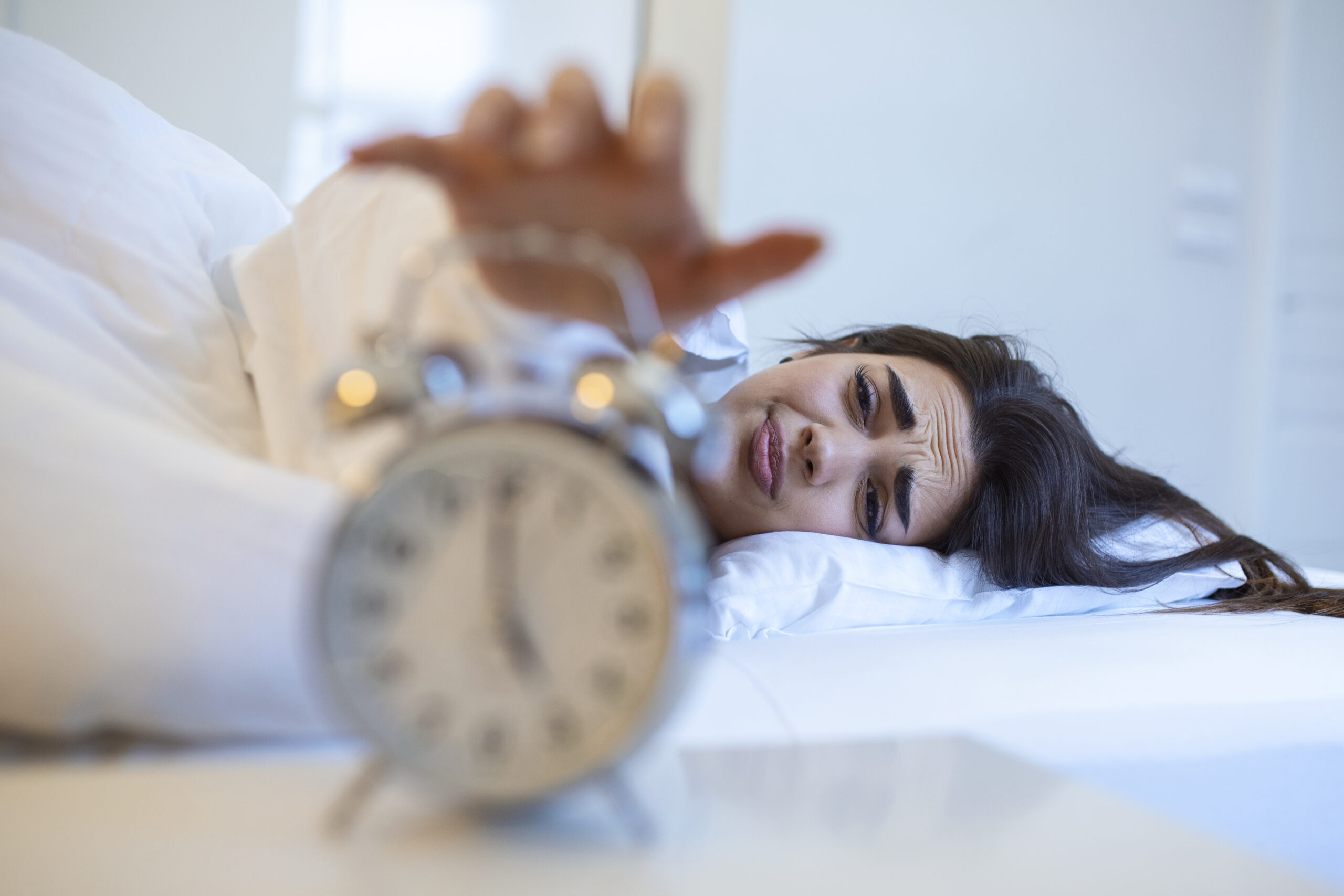 Woman lying in bed turning off an alarm clock in the morning at 5am. Hand turns off the alarm clock waking up at morning, girl turns off the alarm clock waking up in the morning from a call.